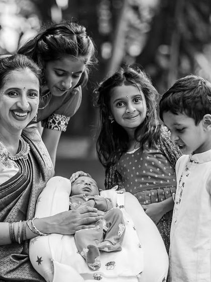 A mother and the older children gather around to admire the family's newest member. This black and white photograph highlights the sweet curiosity and affection of siblings during a naming ceremony.