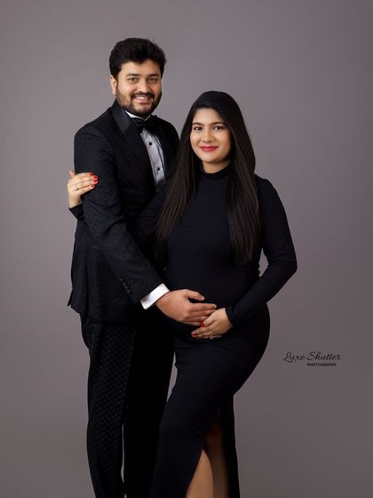 A formal and happy maternity portrait. The husband's tuxedo and the wife's sleek black dress give this studio photo a celebratory and classic feel.