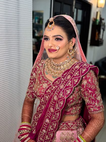 A beautiful bride in a pink and maroon lehenga. Her makeup is soft and elegant, with a focus on clean skin and a matching lip color.