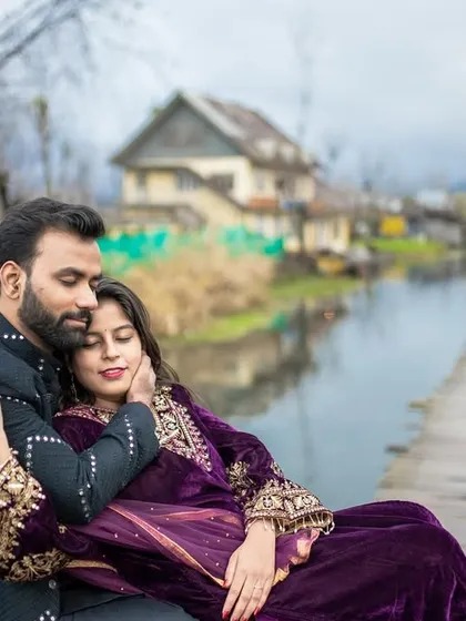 A tender moment captured on a wooden pier by Dal Lake. The bride rests in the groom's arms, with the unique houseboats and calm waters of Kashmir creating a picturesque and romantic setting.