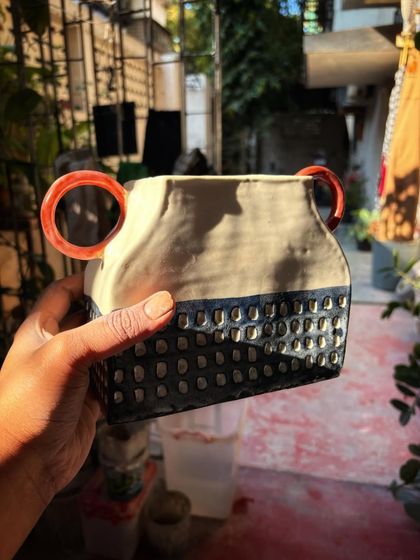 This hand-built vase with its textured blue base and bright red handles was made by Shreya in her beginner phase. It shows a wonderful exploration of form, texture, and color.