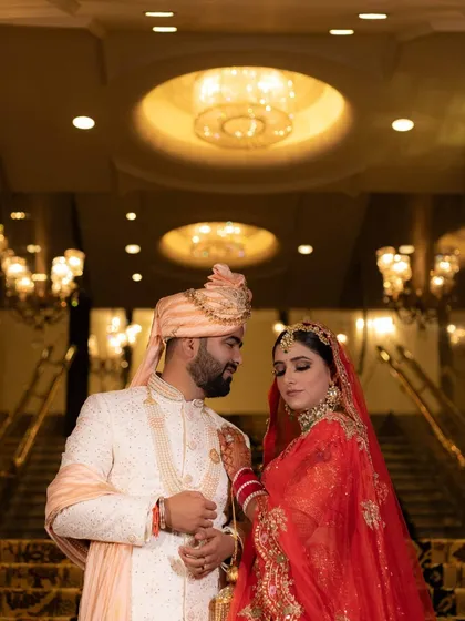 A grand and regal wedding portrait on a staircase. The warm lighting from the chandeliers and the couple's elegant pose create a luxurious and timeless feel.