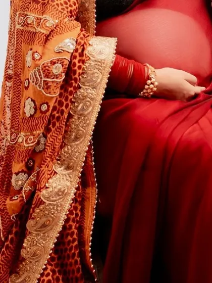A detailed close-up shot focusing on the baby bump, the rich fabric of the saree, and the traditional bangles, symbolizing the life and heritage being celebrated.