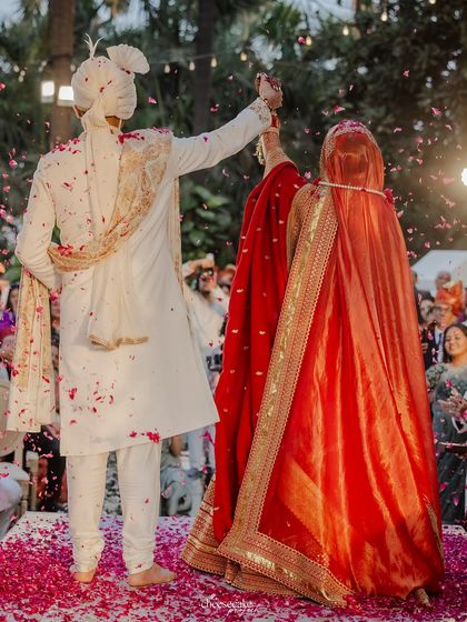A beautiful back shot of the couple during the Varmala, showing the bride's stunning red lehenga and the celebratory petal toss.