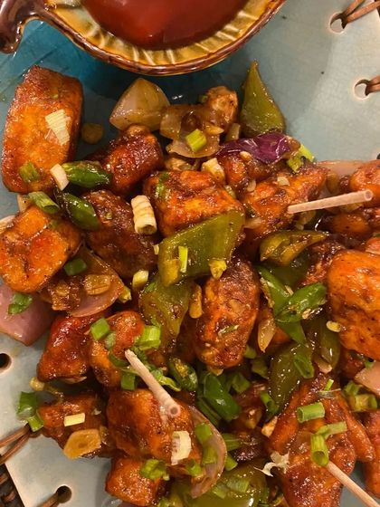 A close-up of our Babycorn Pepper Salt appetizer. Bite-sized pieces of baby corn are fried and tossed with onions, bell peppers, and a generous amount of black pepper for a spicy kick.
