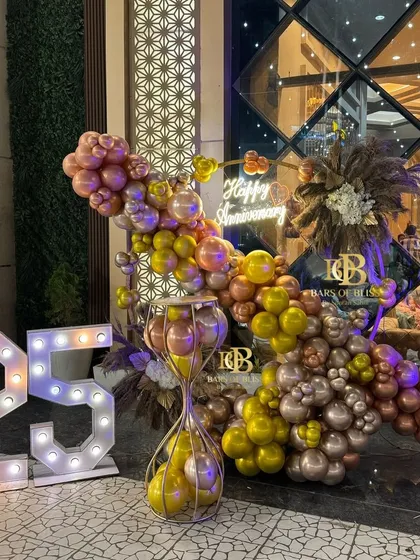 Celebrating a silver jubilee in style. This grand 25th-anniversary decoration combines shimmering metallic balloons, elegant pampas grass details, a 'Happy Anniversary' neon sign, and large marquee numbers for a sophisticated and memorable event.