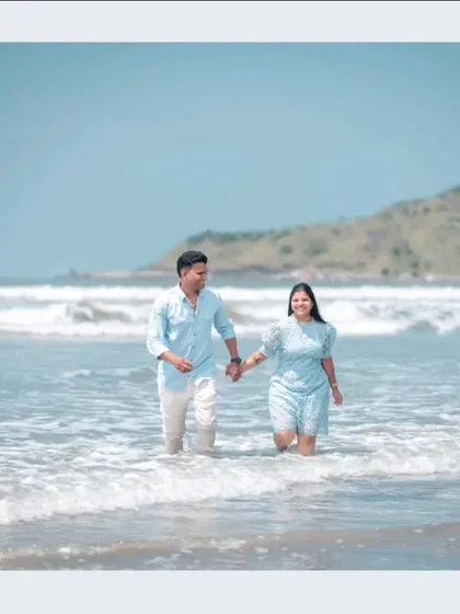 A happy couple holds hands while walking through the gentle waves of the sea, a perfect example of a relaxed and natural beach pre-wedding shoot.