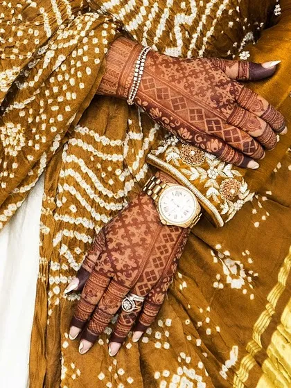 A stylish shot showing how beautifully mehendi pairs with modern accessories like a watch, alongside traditional bandhani fabric.