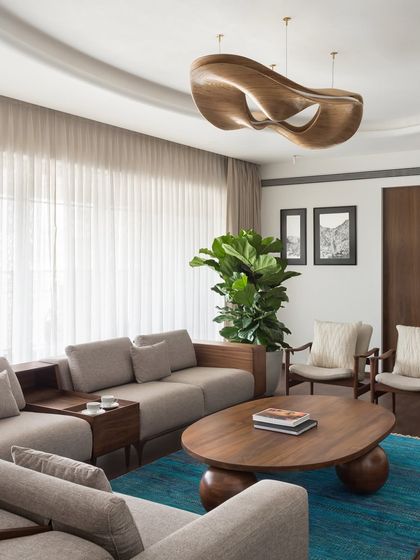 This angle of the West Coast Residence living room highlights the sculptural wooden light fixture and the deep blue rug that grounds the seating area.