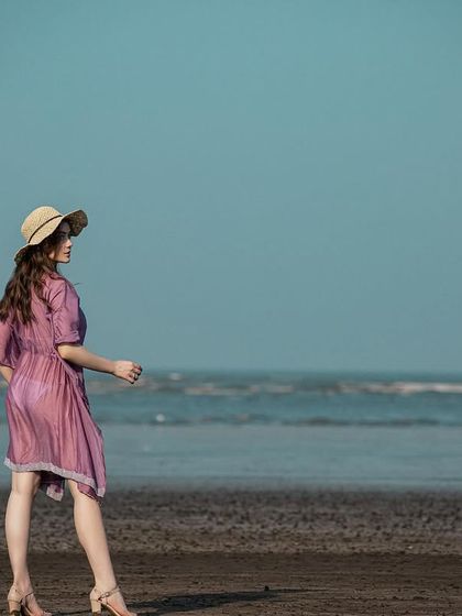 A wide shot that captures the beautiful contrast between the purple kaftan, the blue sky, and the dark sand. The straw hat completes the look.