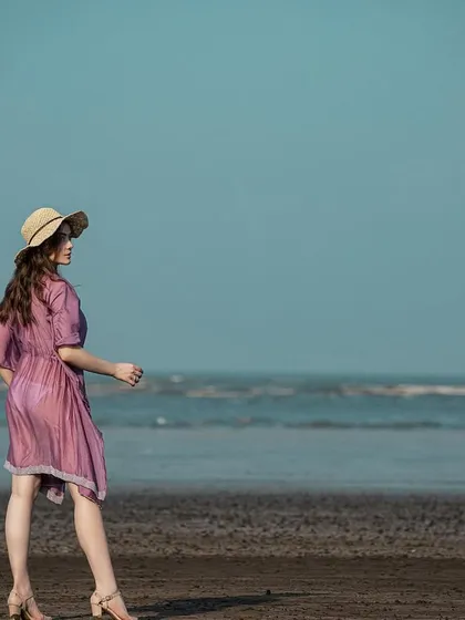 A wide shot that captures the beautiful contrast between the purple kaftan, the blue sky, and the dark sand. The straw hat completes the look.