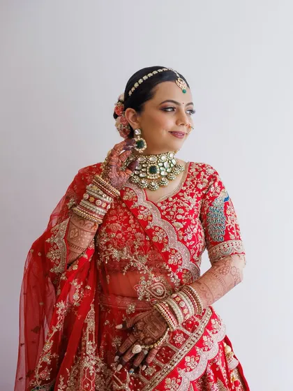 A classic portrait of a bride in red, with her hair in a neat bun adorned with flowers. The makeup is traditional yet fresh, with a focus on defined eyes and radiant skin.