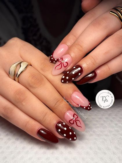 A fun and feminine design combining a deep maroon polish with polka dots and hand-painted bows on a sheer pink base.