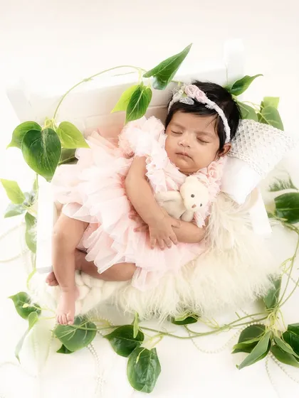 Dressed in a frilly pink dress and holding a tiny teddy, this baby girl looks like a little princess sleeping in her garden-themed bed.