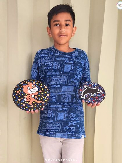 A young boy proudly shows off the fun, character-themed coasters he made during a private dot painting session.