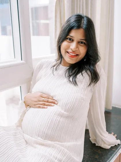 A lovely, bright portrait of the mother-to-be sitting by a window. Her direct, happy gaze at the camera radiates confidence and joy.