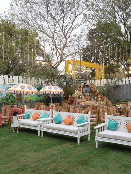 We create relaxed and beautiful outdoor settings for Mehendi functions. This setup includes comfortable white lounge seating with colorful cushions, decorative umbrellas, and string lights for a magical evening ambiance.