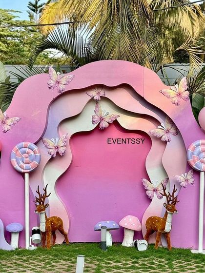 A whimsical, multi-layered pink backdrop with butterfly and deer accents, creating an enchanted forest feel.