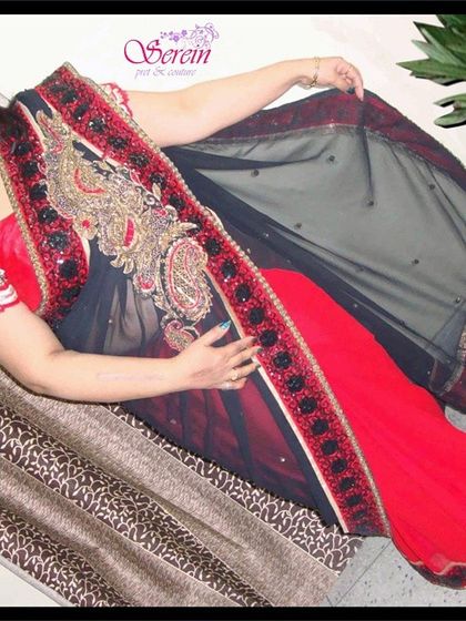 A happy client looking elegant in a custom Serein partywear saree. This red and black net saree is adorned with heavy paisley embroidery along the border, making it a stunning choice for any formal occasion.