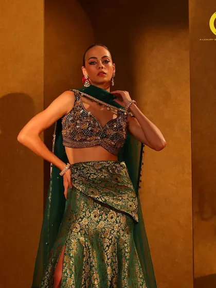 Wrapped in the richness of brocade. This emerald green lehenga features a modern slit skirt and a heavily embellished blouse, perfect for a grand entrance.