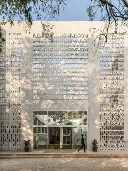 The main entrance of Vidyashilp Academy is framed by large perforated screens. This design provides a grand sense of arrival while functionally serving to shade the glass entrance and ventilate the building's interiors.