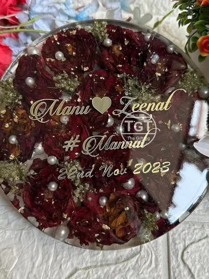 An 8-inch round tabletop piece made with preserved red rose varmala flowers. It's personalized with the couple's names, wedding date, and hashtag in golden text.