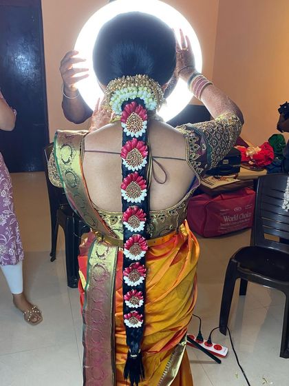 A behind-the-scenes shot of a bride with her floral Muhurtham braid. The ring light highlights the intricate details of the flower arrangement and the neatness of the plait.