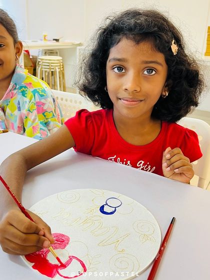 A young girl carefully paints a flower on her nameplate during a fun and creative art party.