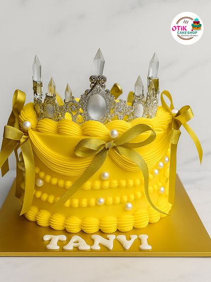 A cake fit for a queen. This vibrant yellow cake is decorated with classic buttercream piping, pearl details, and a stunning silver tiara, making any birthday feel like a royal event.
