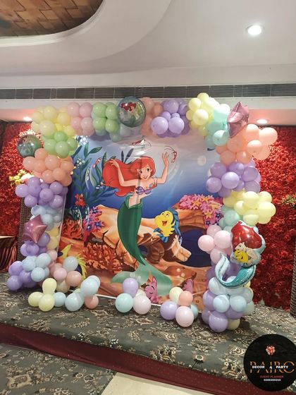 A wider view of the mermaid-themed decoration, showing the full stage setup against a red floral wall.