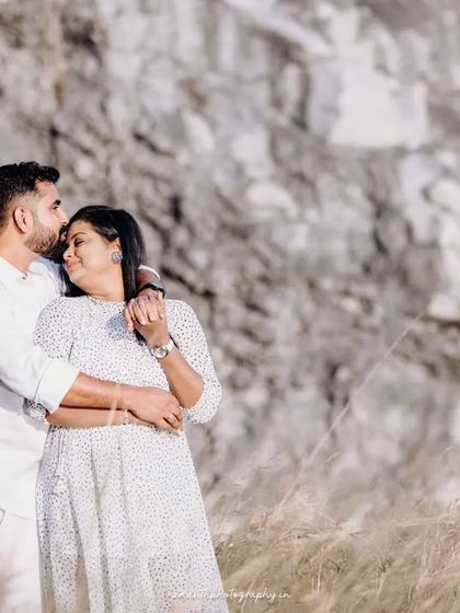 An intimate couple's maternity photo taken outdoors with a natural rock formation as the backdrop. The husband's gentle kiss on her forehead shows their deep connection.