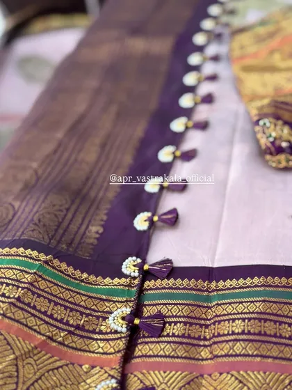 A traditional border with pearl and purple tassels, adding a classic touch to this purple and gold silk saree.