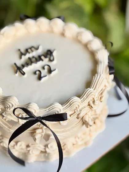 Dripping in old-world charm. A close-up of this vintage dream cake, with its off-white buttercream, intricate piping, and chic black ribbons.