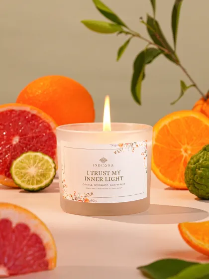 A citrus-scented candle surrounded by fresh oranges and grapefruit. The vibrant colors and fresh fruit make the product look zesty and refreshing.
