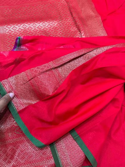 The plain red blouse piece with a simple green and gold border, belonging to one of our rich Banarasi silk sarees.