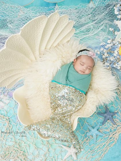 A mermaid princess from the deep blue sea. This creative setup features a newborn with a sparkling mermaid tail, sleeping in a giant seashell.