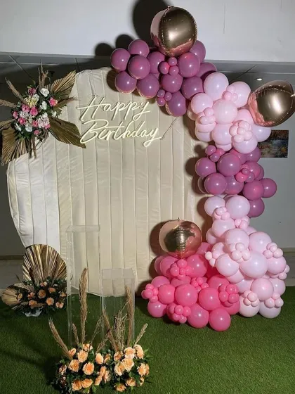 A chic and bohemian-inspired setup with a cream-colored fabric backdrop, a pink balloon arch, and pampas grass floral arrangements.