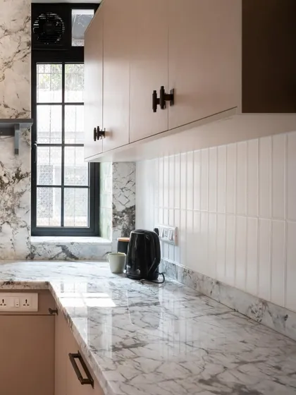The way the light hits the marble countertop in this compact kitchen is just beautiful. The combination of natural stone, simple white tiles, and a dark framed window creates a serene and timeless feel.