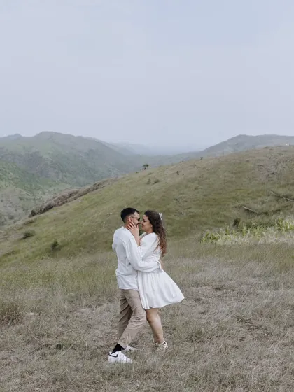 An embrace in the middle of a vast, green valley. This wide shot emphasizes the scale of the landscape and the intimacy of the couple's moment.