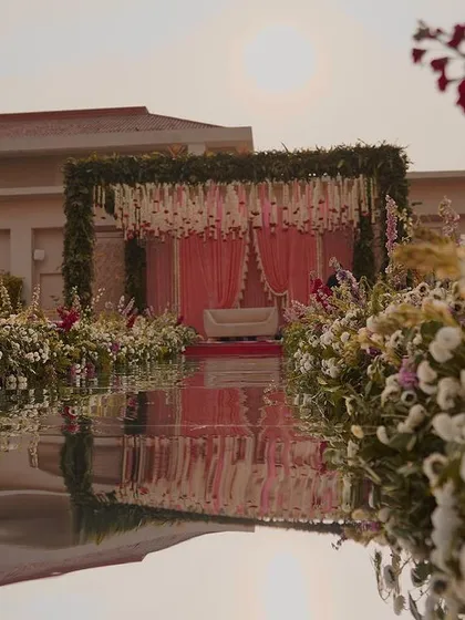 We love creating dreamlike settings, like this serene daytime mandap. The floral aisle, reflected perfectly in the water, leads to a stage adorned with fresh blooms and delicate pink drapes, making for a truly picturesque wedding ceremony.
