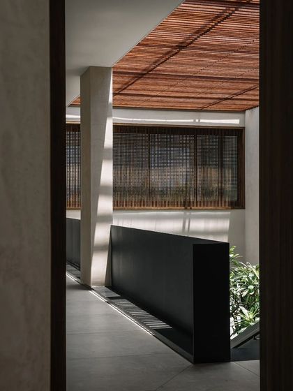 The interplay of light and shadow is a key theme in this home. Here, sunlight filters through a bamboo ceiling, casting linear patterns across the corridor and highlighting the home's minimalist architecture.