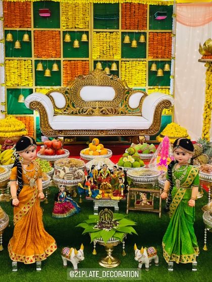 A full view of a traditional baby shower setup with a yellow and green checkered backdrop. The decor includes two large dolls, a central doll scene, and a complete arrangement of plates.