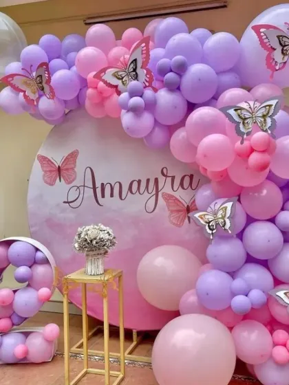 A beautiful butterfly-themed second birthday party with a soft pink and purple palette. This outdoor setup includes a personalized circular backdrop, an organic balloon arch, and a balloon-filled marquee number '2'.