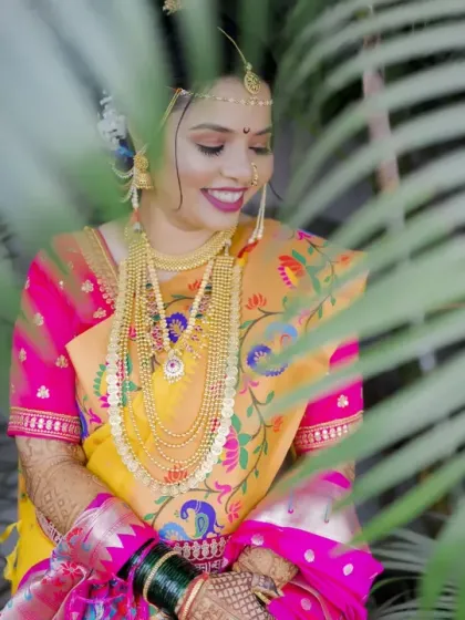 A shy, happy smile from the bride, peeking through lush green leaves for a natural and soft portrait.