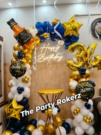 A fun and stylish birthday decoration for an adult, featuring a blue, white, and gold balloon arch with a whiskey bottle foil balloon and a neon sign.