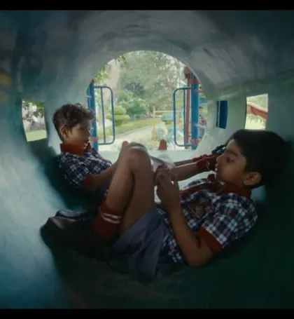 Two boys in their school uniforms, sharing a moment in a playground tunnel. The styling is simple and doesn't distract from the emotional core of the scene.