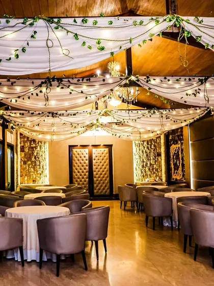 A rustic and elegant indoor venue decoration. We draped the ceiling with white fabric and intertwined fairy lights and green vines, creating a warm and magical ambiance for a dinner or reception.