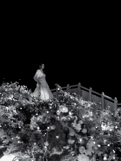 A bride stands amidst a sea of flowers, illuminated by fairy lights. This black and white shot is pure magic, a testament to our belief in creating dreamlike, romantic settings.