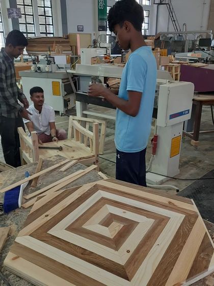 A student project combining multiple skills: in the foreground, a tabletop with a spiral inlay pattern, and in the background, the frame of a small chair.