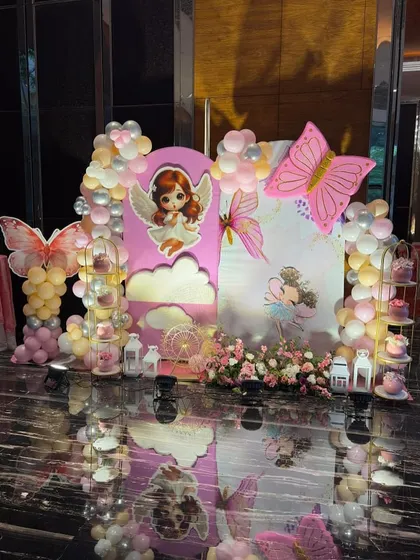 An angelic butterfly theme with a pink backdrop featuring a cute angel character and butterfly wings. The dessert stands are filled with treats, and the whole area is surrounded by pastel balloons.